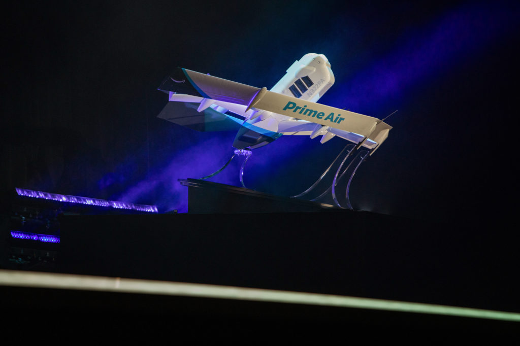 Modelo de avião da Budweiser suspenso, iluminado por luz azul em palco escuro.