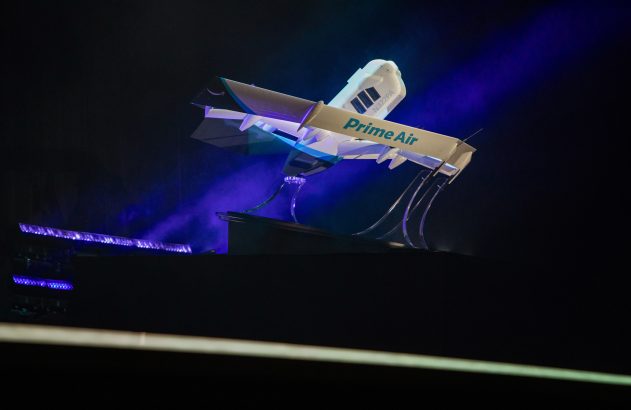 Modelo de avião da Budweiser suspenso, iluminado por luz azul em palco escuro.