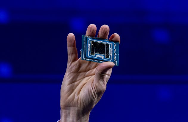 Mão segura um chip eletrônico retangular contra um fundo azul desfocado.