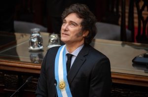 Javier Milei, presidente da Argentina, com faixa presidencial azul e branca, olha para o alto em evento.