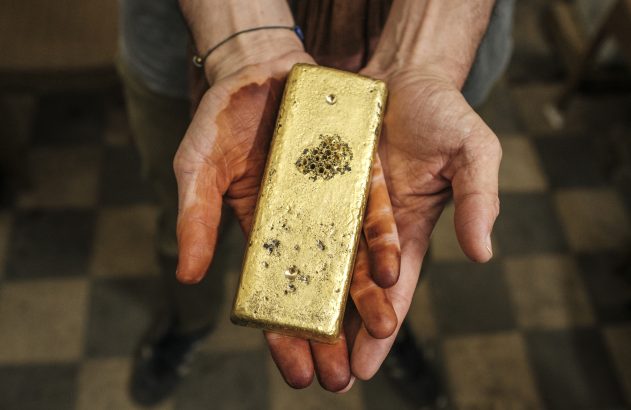 Mãos segurando um bloco retangular de manteiga ou queijo artesanal com ervas.