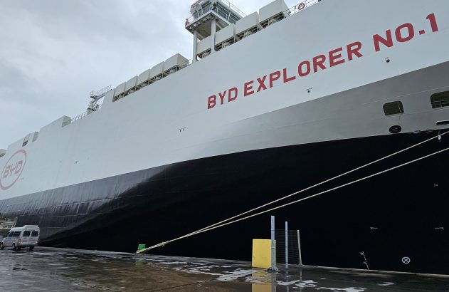 Navio BYD EXPLORER NO. 1, com logo BYD, atracado em porto com chão molhado e vans próximas.