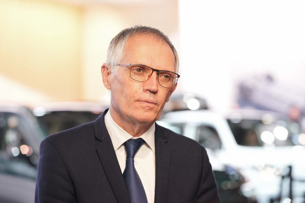 Homem de terno e óculos olhando para o lado. Fundo desfocado com carros e luzes.