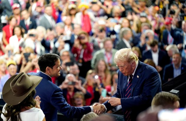 Donald Trump aperta a mão de um homem, com multidão ao fundo.