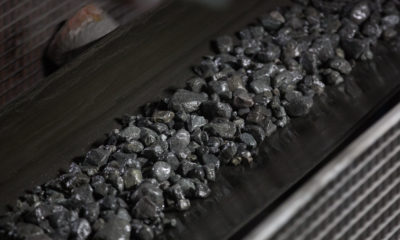 Minério escuro e úmido em esteira transportadora industrial.