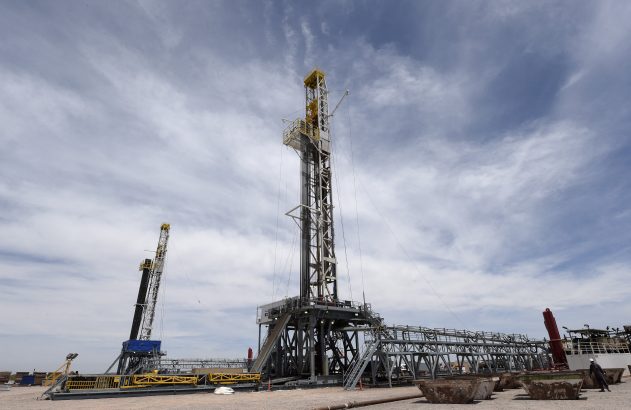 Duas sondas de perfuração em campo de petróleo, uma grande central e outra menor à esquerda, sob céu nublado.