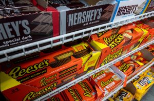 Doces variados, incluindo barras Hershey's e Reese's, expostos em prateleiras de metal de uma loja.