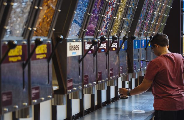 Pessoa servindo-se de doces de uma série de dispensadores, como Hershey's Kisses.