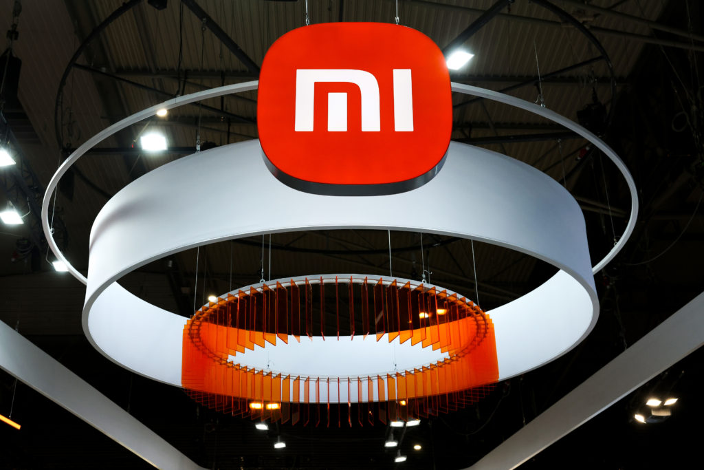 Logotipo da Xiaomi (MI) vermelho e branco suspenso, com anéis brancos e um anel interno laranja.