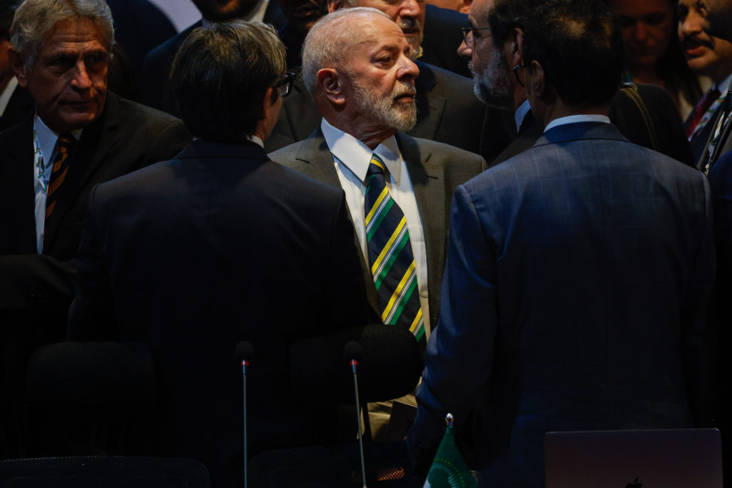 Presidente Lula, de terno e gravata listrada, conversa em grupo formal.