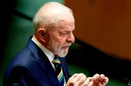 Lula, de terno azul e gravata verde e amarela, discursando em público com as mãos visíveis.