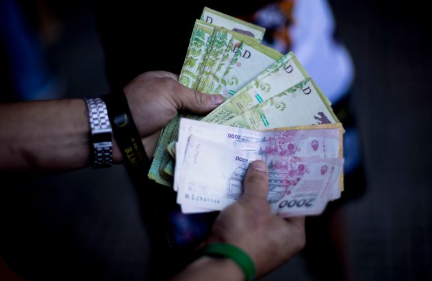 Duas mãos seguram e contam maços de notas de dinheiro, verdes e de 2000.