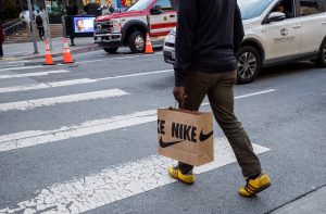 Homem atravessa faixa de pedestres com sacola Nike e tênis Adidas amarelos.