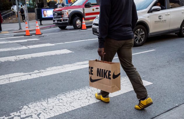 Homem atravessa faixa de pedestres com sacola Nike e tênis Adidas amarelos.