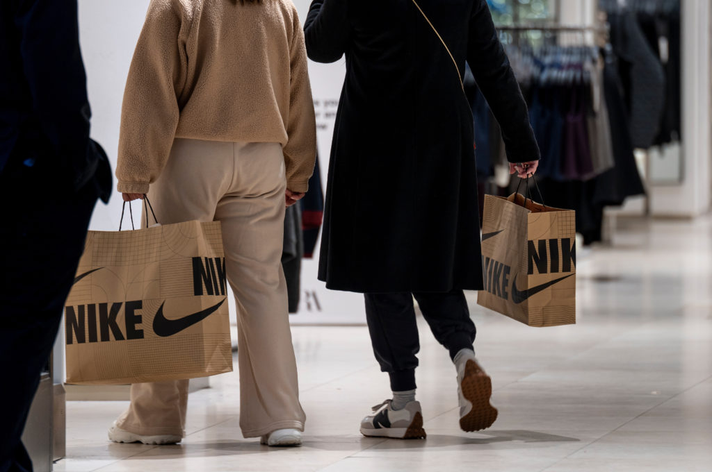 Duas pessoas de costas carregam sacolas da Nike em um shopping.
