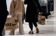Duas pessoas de costas carregam sacolas da Nike em um shopping.
