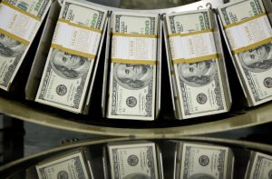 Maços de notas de US$100 em uma esteira de contagem, com reflexos visíveis.
