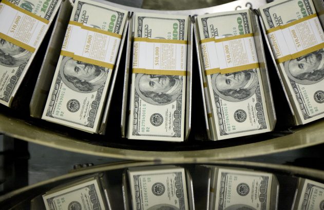 Maços de notas de US$100 em uma esteira de contagem, com reflexos visíveis.