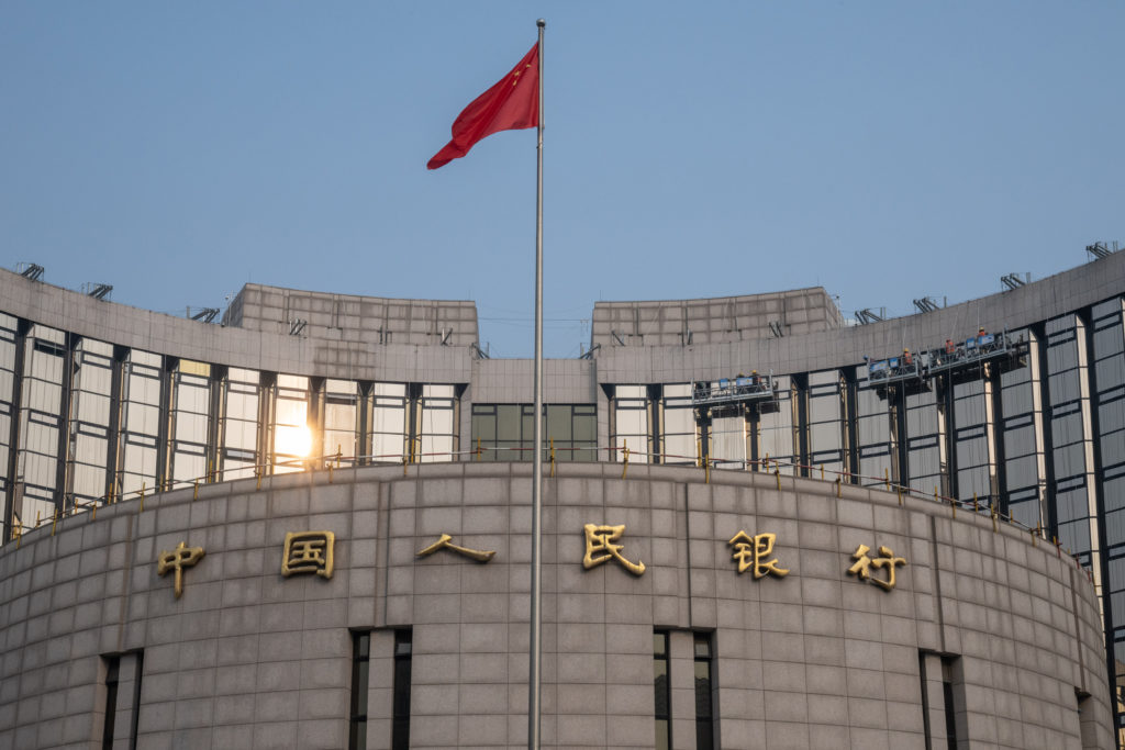 Edifício curvo do Banco Popular da China com a bandeira chinesa tremulando no topo.