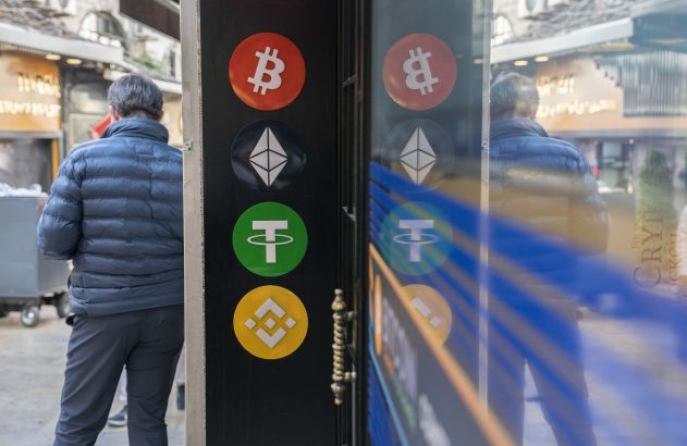Homem de costas em rua, próximo a painel refletivo com logos de criptomoedas: Bitcoin, Ethereum, Tether e Binance.