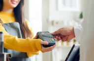 Imagem de uma pessoa segurando uma máquina de cartão em um ambiente comercial, prestes a realizar um pagamento.