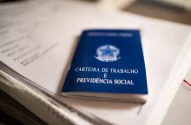 Carteira de trabalho azul sobre um caderno, símbolo de emprego e direitos trabalhistas no Brasil.