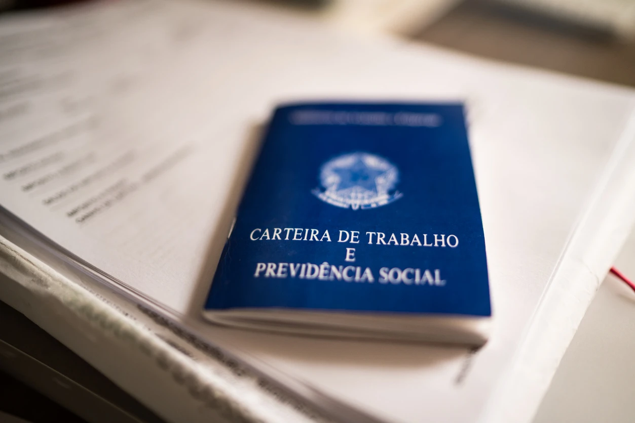 Carteira de trabalho azul sobre um caderno, símbolo de emprego e direitos trabalhistas no Brasil.