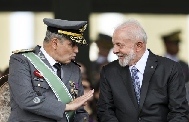 General Tomás (fardado) gesticula enquanto conversa com Lula, que sorri.