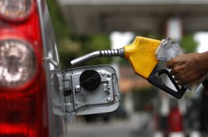 Mão com bico de combustível amarelo abastecendo carro vermelho.