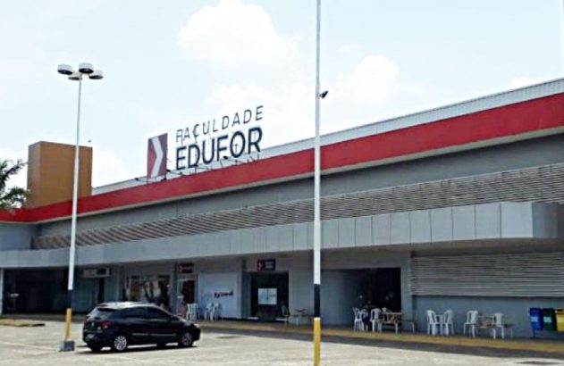 Entrada da Faculdade Edufor com fachada cinza e vermelha. Letreiro grande visível. Pátio com carros estacionados.