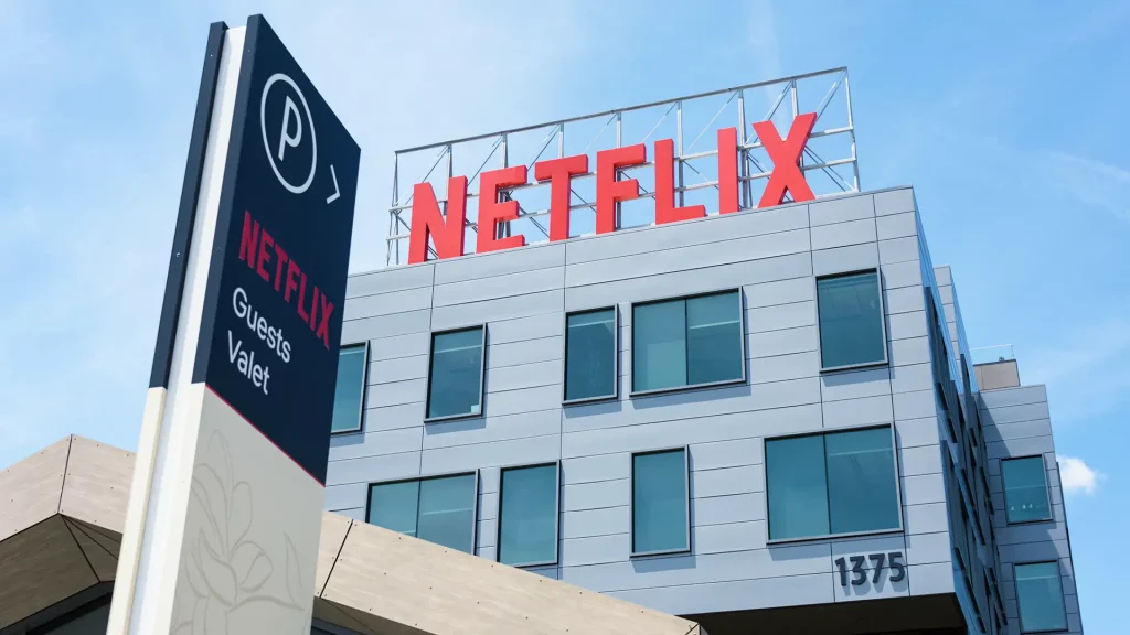 Um edifício moderno da Netflix com fachada cinza, diversas janelas e letreiro vermelho, em um dia ensolarado.