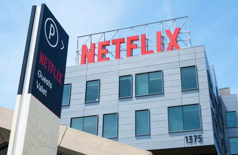 Um edifício moderno da Netflix com fachada cinza, diversas janelas e letreiro vermelho, em um dia ensolarado.