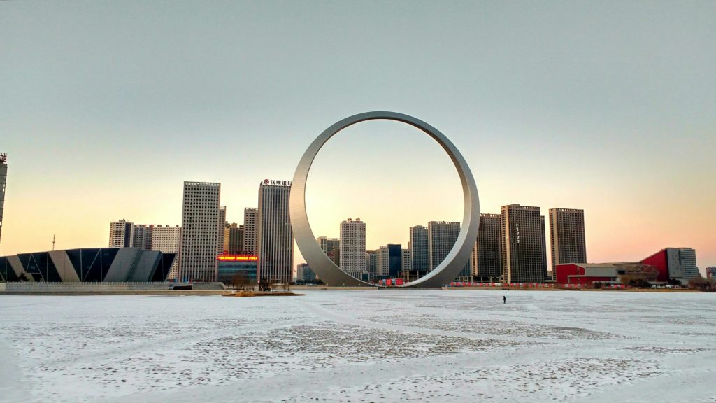 Paisagem urbana moderna com anel gigante e prédios, chão claro.