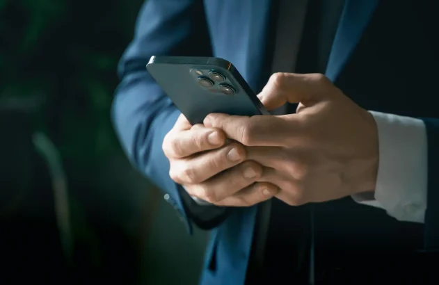 Em um ambiente interno suavemente iluminado, uma pessoa em um terno azul escuro segura um celular moderno com múltiplas lentes.