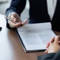 Duas pessoas em uma reunião profissional com documentos e símbolos jurídicos ao fundo.