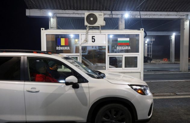 Carro branco com duas pessoas em guarita de fronteira entre Romênia e Bulgária, com o número "5", à noite.