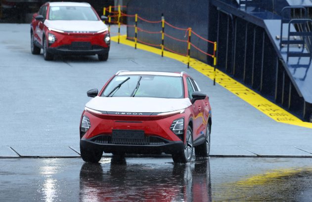 Carros vermelhos OMODA em rampa molhada. Um em destaque com limpadores levantados, outro carro ao fundo.