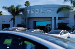 Fachada de um prédio Tesla com o letreiro "TESLA" e a indicação "SERVICE". Carros Tesla estacionados em frente.
