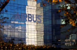 Fachada de vidro de prédio moderno reflete 'AIRBUS', céu, nuvens e folhagem.
