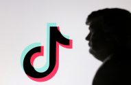 Um perfil em silhueta observa o logo do TikTok em preto, ciano e rosa em fundo claro.