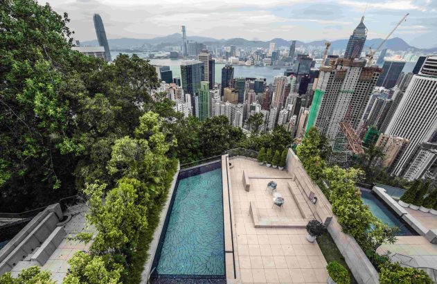 Vista panorâmica de Hong Kong com arranha-céus, porto, montanhas e uma piscina com terraço verde.