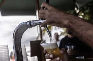 Pessoa despeja cerveja gelada de torneira cromada em copo plástico.
