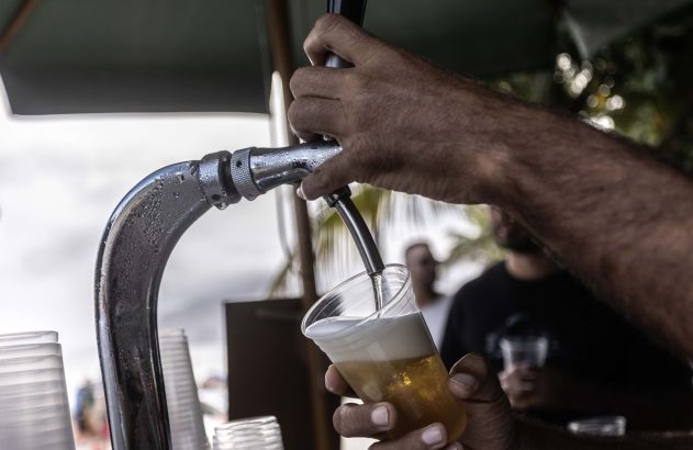Pessoa despeja cerveja gelada de torneira cromada em copo plástico.