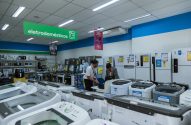 Dois homens interagem em balcão de loja de eletrodomésticos da Magalu, exibindo geladeiras e máquinas de lavar.