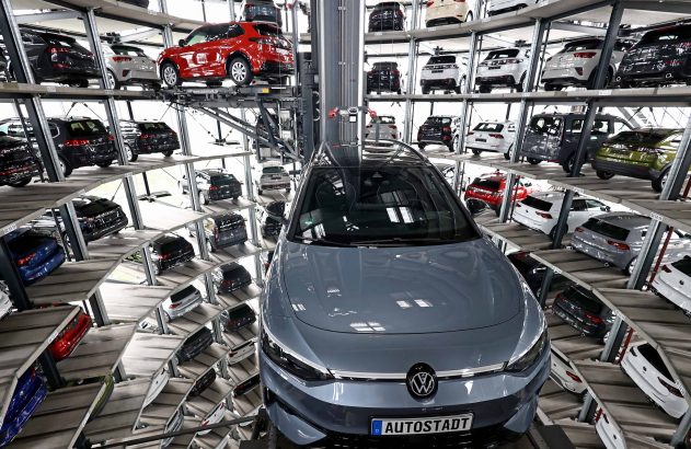 Um Volkswagen cinza à frente, com dezenas de carros em uma torre de armazenamento automotiva robótica na Autostadt.