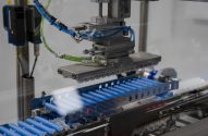 Automação industrial: braço robótico sobre esteira com cilindros azuis sendo processados.