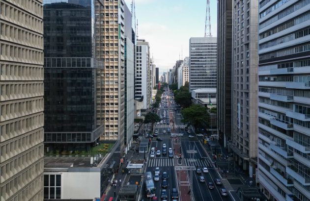 Vista aérea de avenida movimentada ladeada por arranha-céus, com tráfego intenso e pedestres.