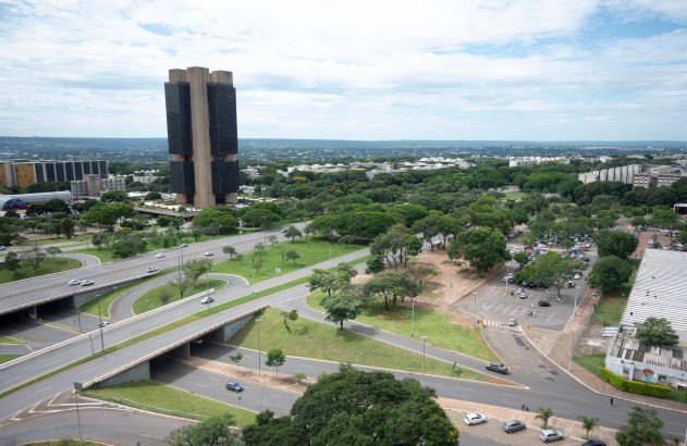 Vista aérea do Banco Central em Brasília. Complexo viário, carros e vasta área verde urbana sob céu nublado.
