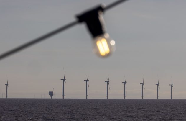 Parque eólico offshore em linha no mar, com uma lâmpada acesa e desfocada em primeiro plano.