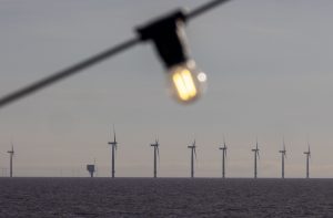 Parque eólico offshore em linha no mar, com uma lâmpada acesa e desfocada em primeiro plano.